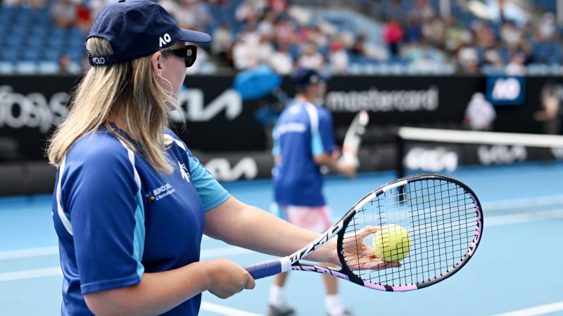 A female athlete prepares to serve a yellow ball used in blind and low vision tennis