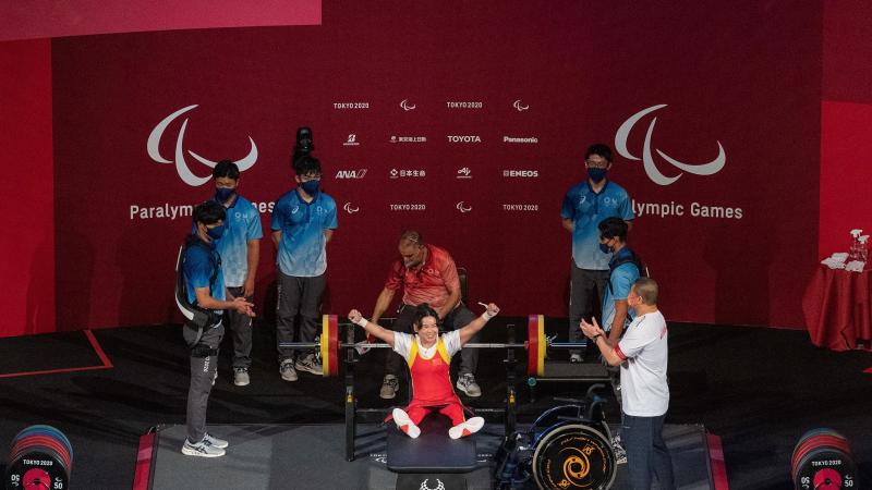 A female Para powerlifter celebrated on stage with five people around her