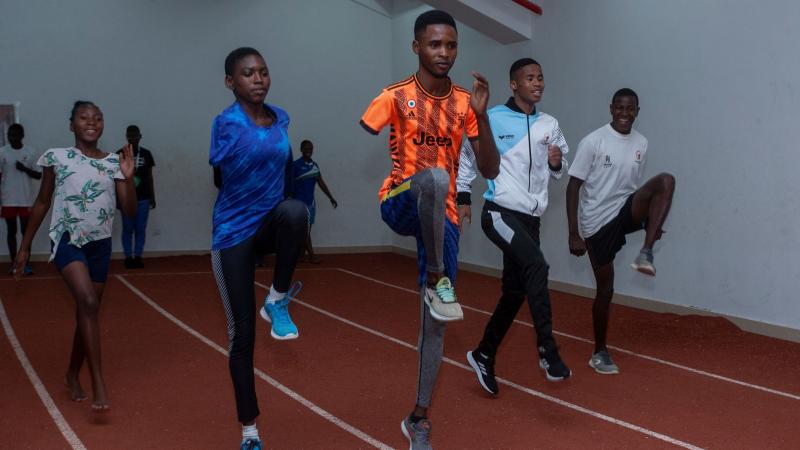 Five African athletes train, doing upward kicks, on an indoor track.