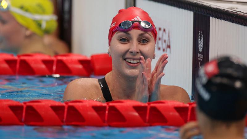 A female Para swimmer claps her hands in the pool after finishing her race.