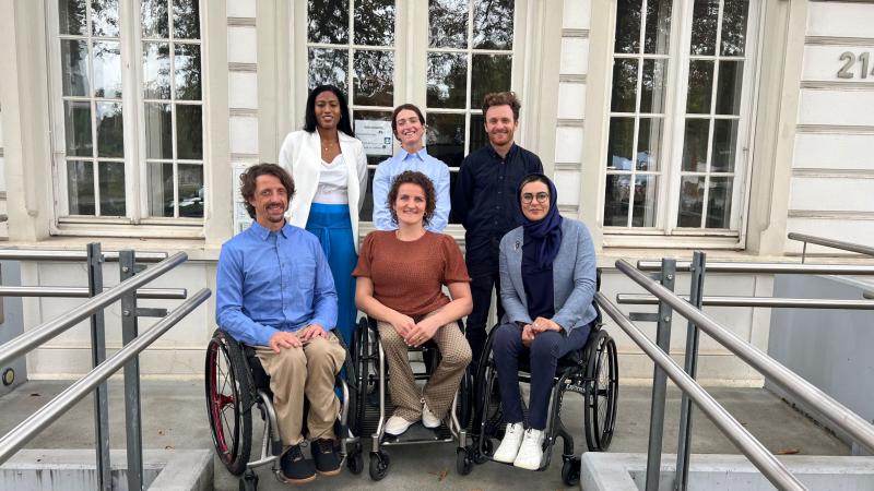 Six athletes, three standing in the back and three in wheelchairs at the front, pose for a photo in front of the IPC headquarters.