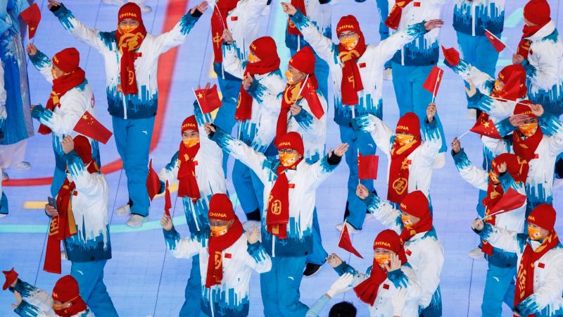 About 20 people march in the main stadium of the Beijing 2022 Games while waving small Chinese flags.