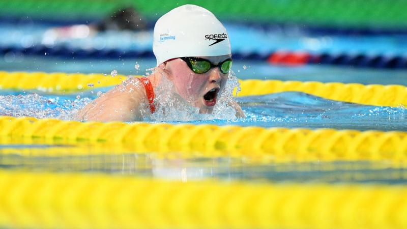 A female swimmer with a white cap swimming backstroke