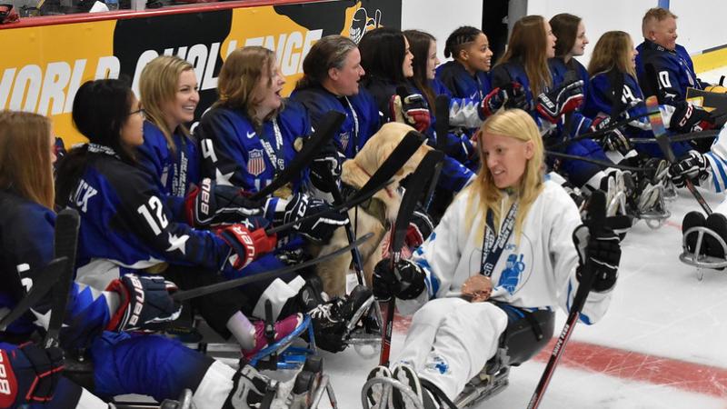 Female athletes in blue jersey are on the ice, while a female athlete in white jersey passes by.