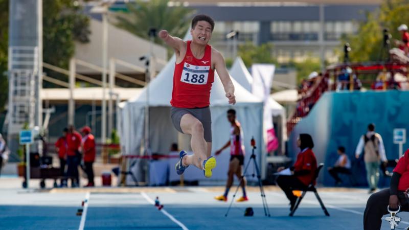A one-armed man jumping in a long jump competition in a blue athletics track