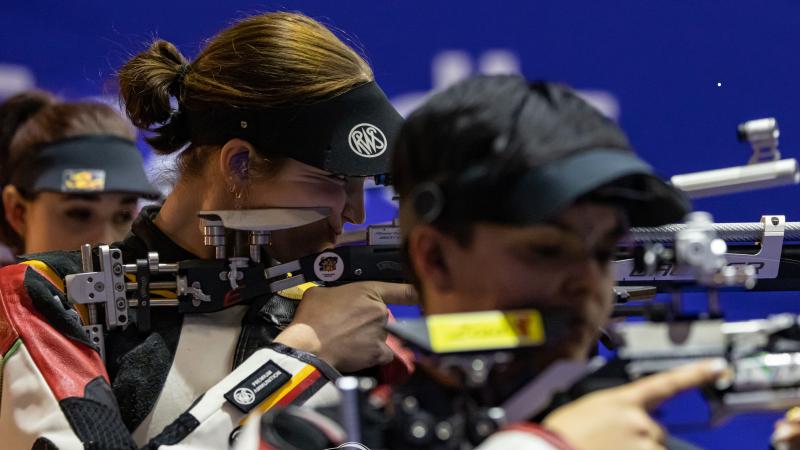 Three women competing in rifle shooting Para sport event indoors