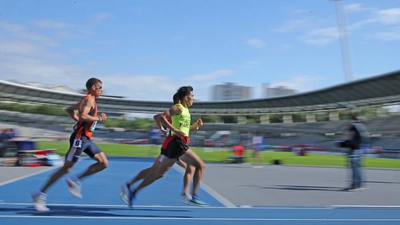 Three men running in a blue athletics track during a Para athletics event at Charlety Stadium in Paris