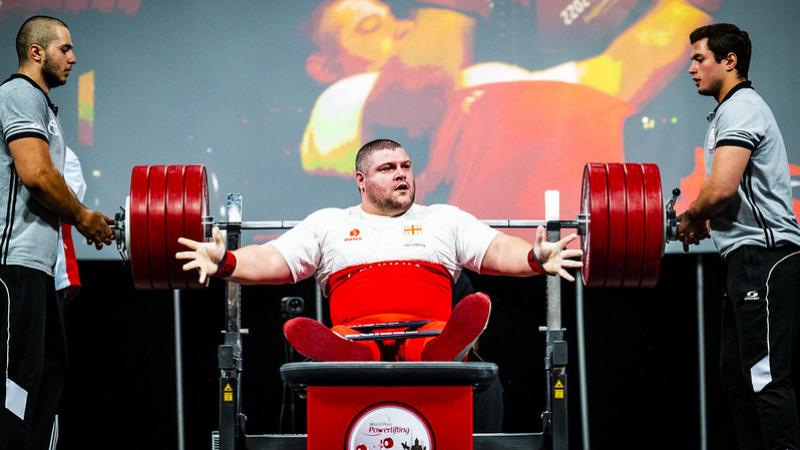 A male powerlifter in a bench press with two men standing next to him