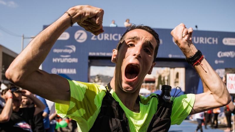 A male runner with cerebral palsy raises his hands in the air at the finish line of the Barcelona Marathon.