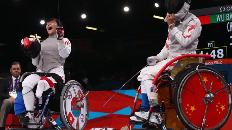 A female wheelchair fencer celebrates by taking her mask off with a shout after a winning bout.