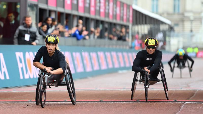 A female wheelchair racer crossing the finish line ahead of another racer in a street marathon