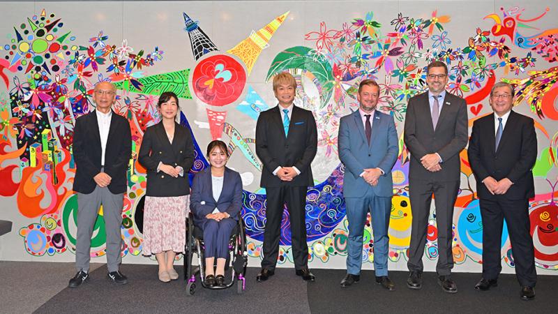 Seven people pose for a photograph in front of an artwork.