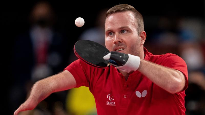 A male athlete wearing a red T-shirt plays table tennis