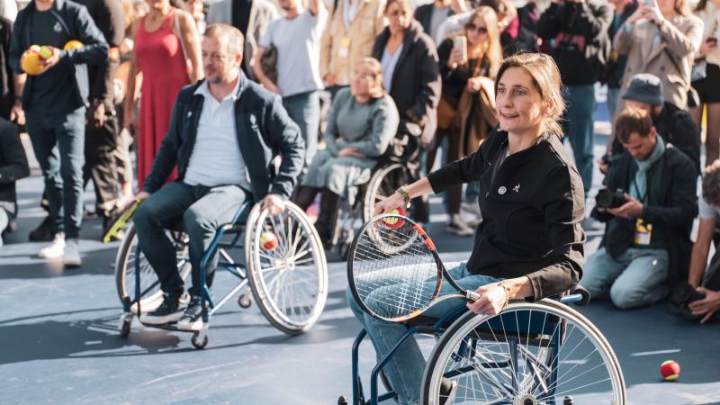 A woman and a man on a wheelchair holding tennis racquet.