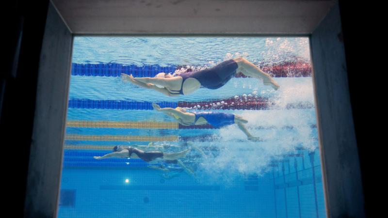 An image of three female Para swimmers from a window at the bottom of the pool