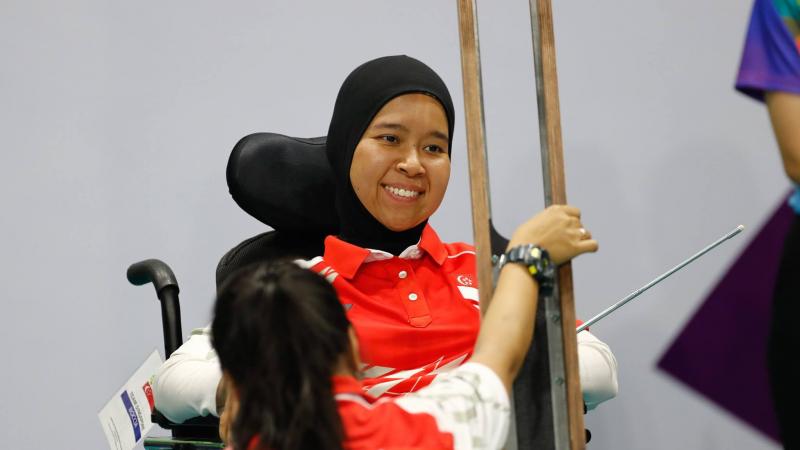 A female boccia athlete looks at her boccia ramp, while her assistant holds it.