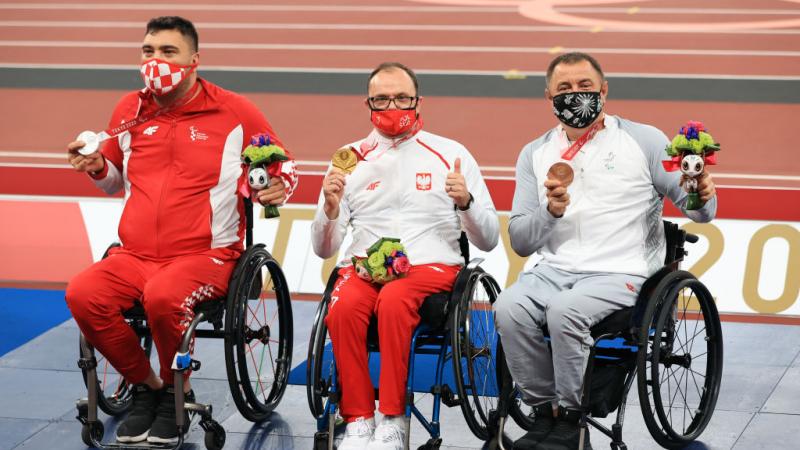 Three male athletes on wheelchairs posing for a photo with medals.