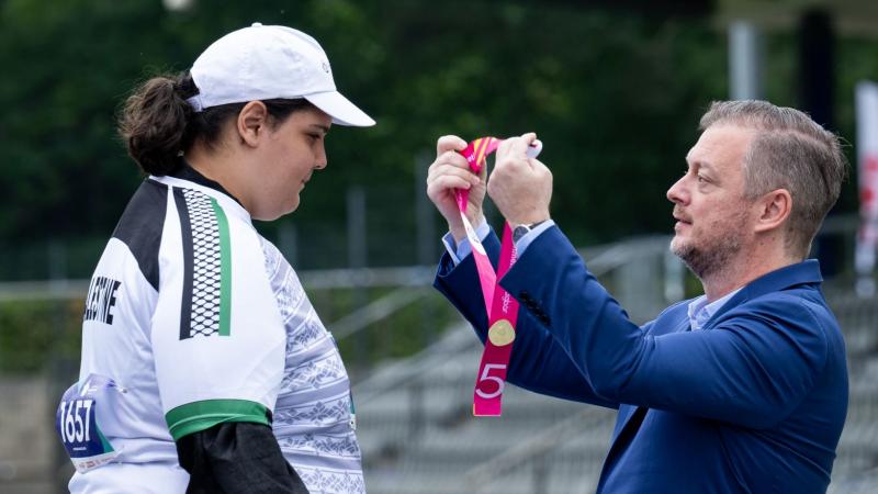 A man wearing a blue suit presents a medal to a female athlete.