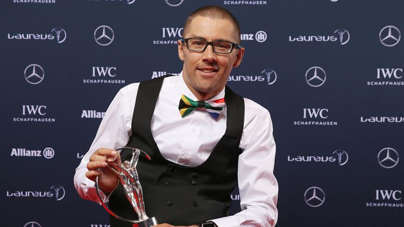 A male athlete poses at an awards ceremony with a silver trophy.