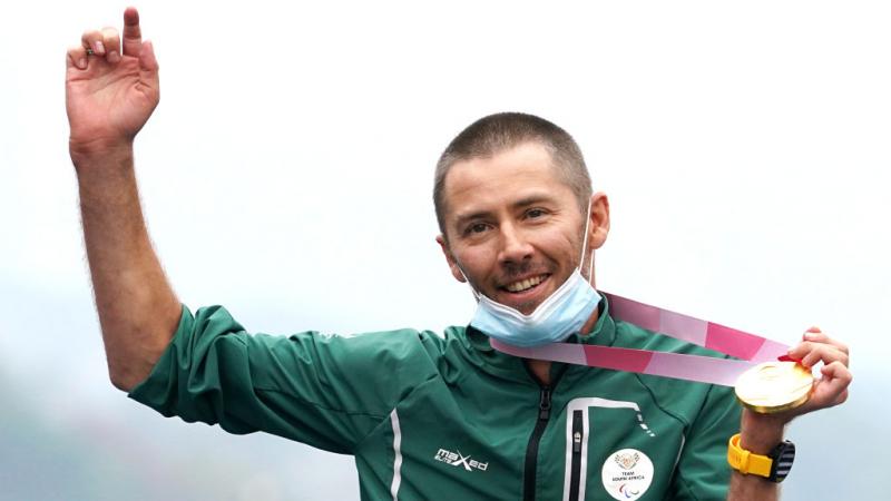 A male athlete raises his right arm in celebration while holding a gold medal with his left hand.