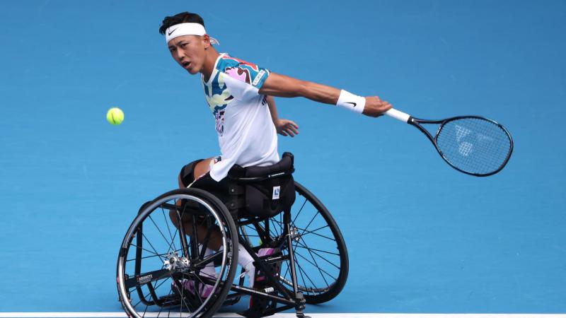A male wheelchair tennis player hits a ball.