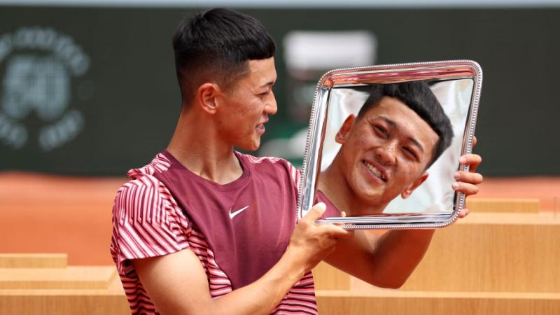 A male athlete holds the French Open trophy. His face is reflected on the silver trophy. 