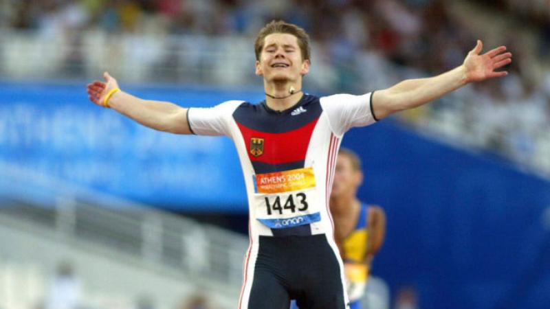 A male runner with a prosthetic leg celebrates with his arms wide open as he finished a race.