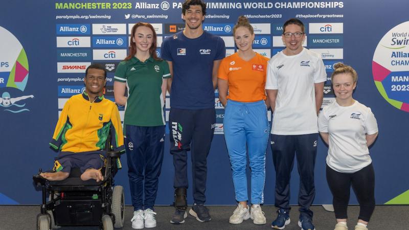 A male wheelchair posing for a picture next to a woman and a group of two men and other two women