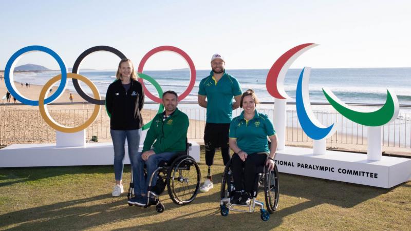 two wheelchair athletes and two athletes with prosthetics standing in front of the Paralympic and Olympic symbols 