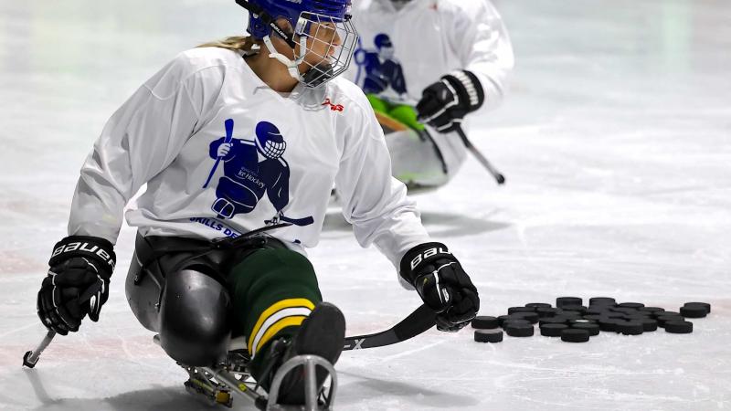 A female Para ice hockey player on an ice rink followed by a male player