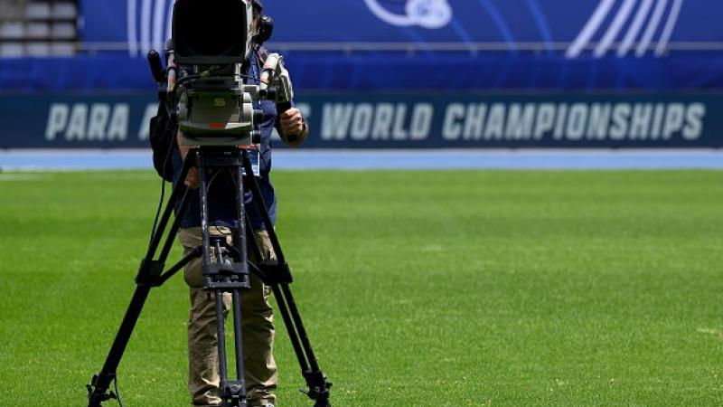 A TV camera on a grass pitch in an athletics stadium