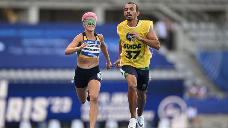 A female runner wearing green blindfolds competes with her guide runner