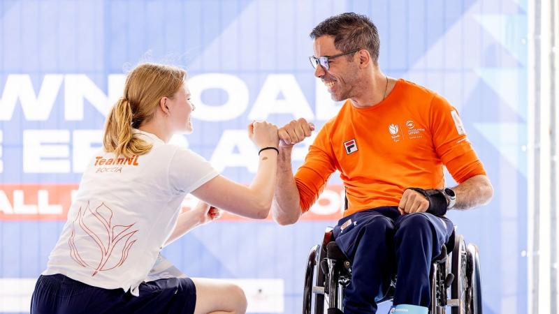 A male athlete and a female official wearing a Tshirt that says "Team NL boccia" celebrate