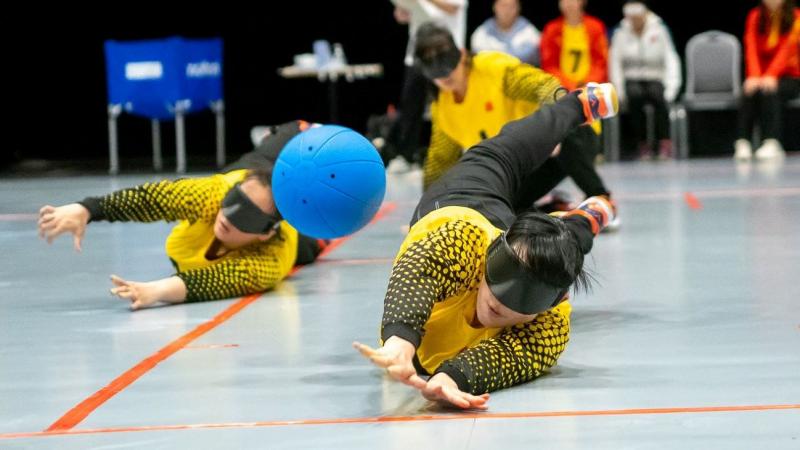 Two female athletes block a blue ball during a goalball match