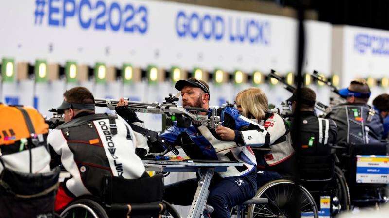 A group of five male and female rifle shooters in wheelchairs in a shooting range