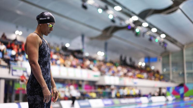 A female swimmer standing next to a pool in a crowded venue