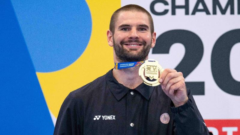 Para badminton player Lucas Mazur holding up his gold medal and smiling