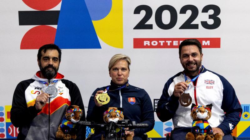 A woman in a wheelchair between two men on a podium