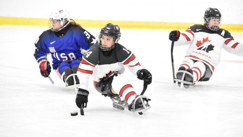 A Canadian female Para ice hockey player on ice followed by a USA player