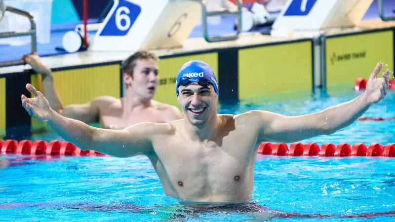 A male swimmer with his arms stretched in a pool with another swimmer in the background