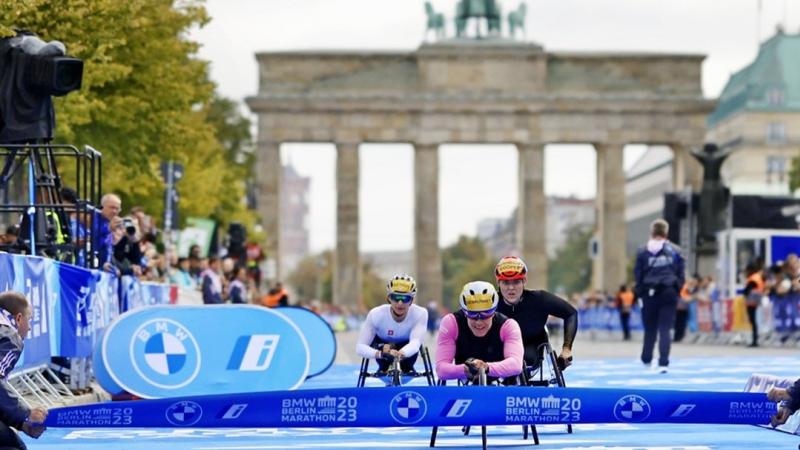 A female wheelchair racer crossing the finishing line of the Berlin Marathon ahead of two competitors