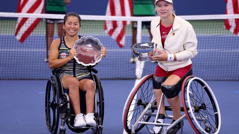 Two female wheelchair tennis athletes pose for a photo on the tennis court with their silverware