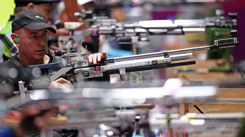 A male rifle shooter in the middle of other athletes in a shooting range