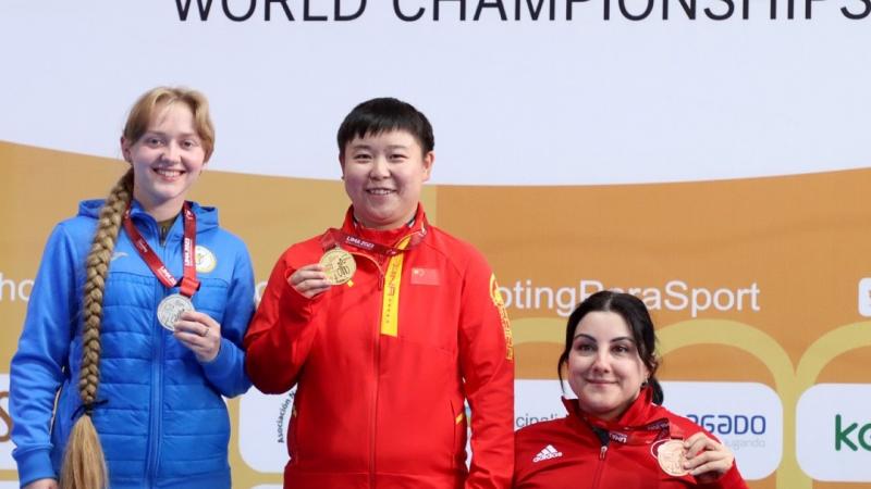 Two women standing next to a seated woman showing their medals