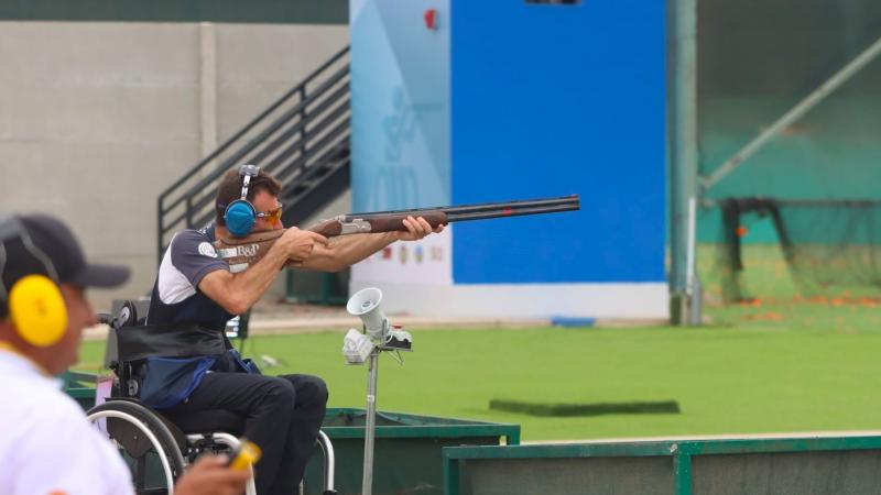 A man in a wheelchair in an outdoor Para trap shooting event