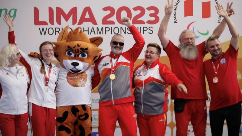 Three women and three men on a podium with a mascot