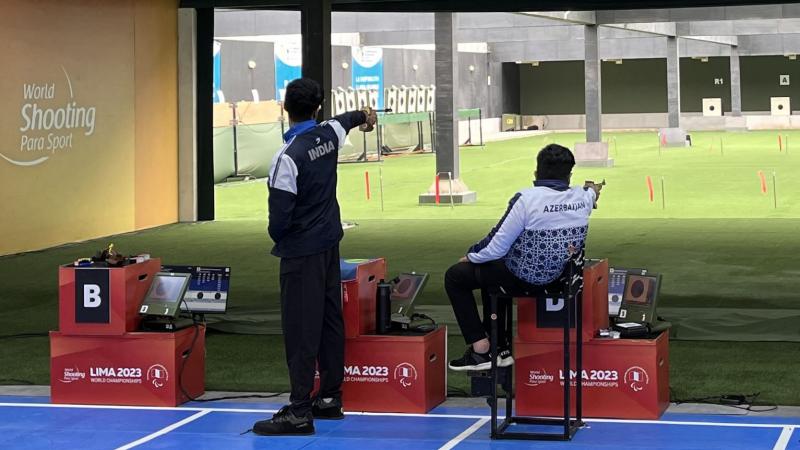 A standing man and a man in a wheelchair competing in a shooting range