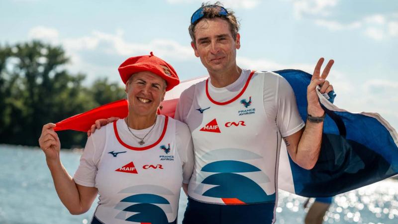 A male and a female Para rower pose for a photograph while holding the French flag.