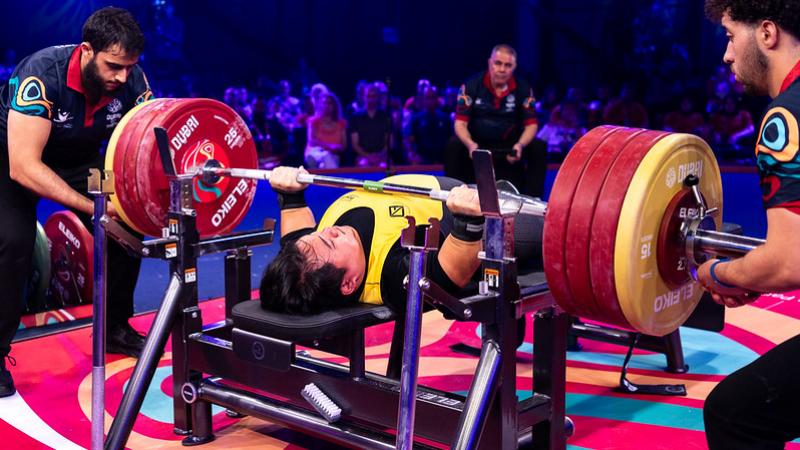 A short stature man lifting a bar in a Para powerlifting competition