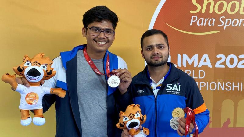 Two athletes holding medals and a mascot plush toy 